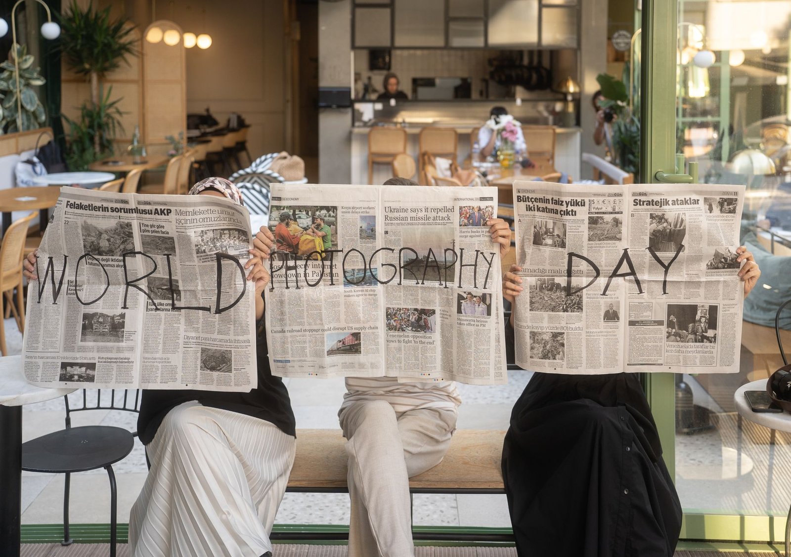 Three people holding newspapers promoting World Photography Day in a cozy Ankara café. — Enhance Your Beauty with Botox Injec