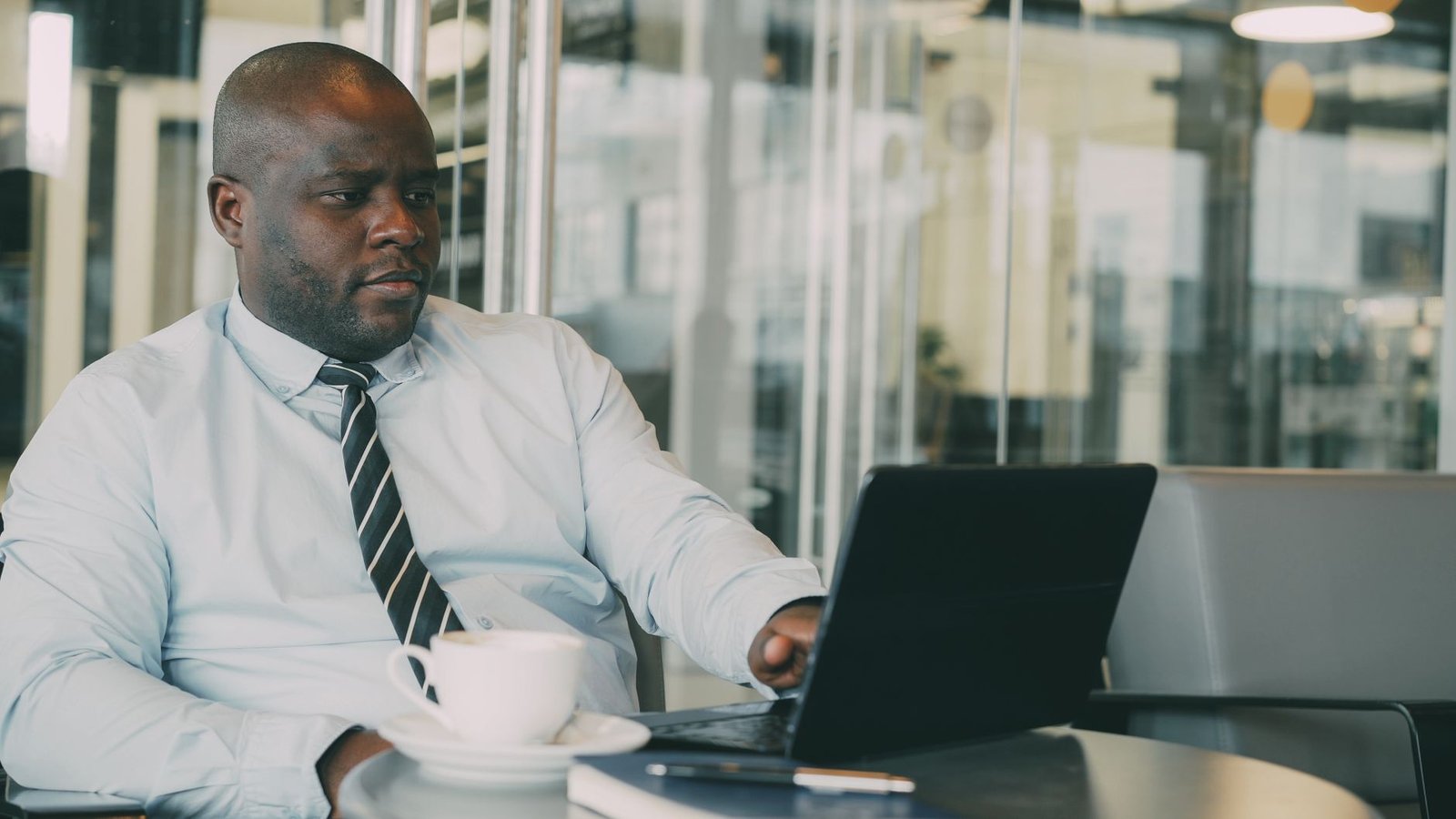 Focused businessman uses laptop in stylish cafe, sipping coffee. Perfect for business or lifestyle themes. — Mileage reimburs