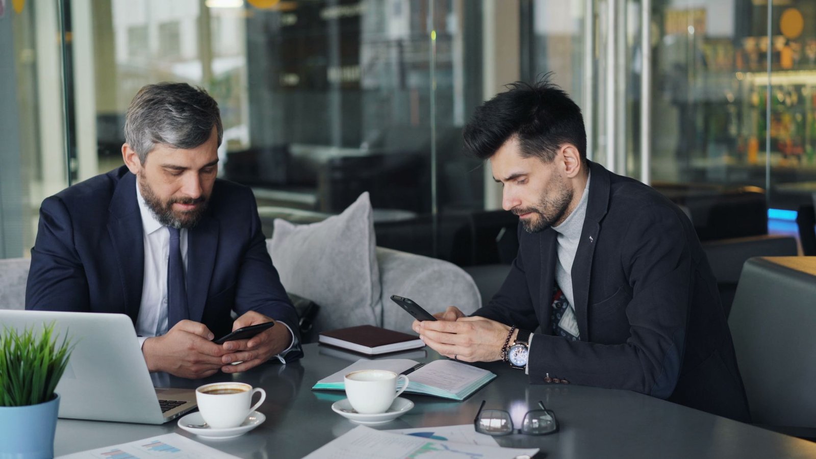 Two businessmen in a cafe working on smartphones and laptops, engaged in a meeting. — Student Housing Management Software Tha